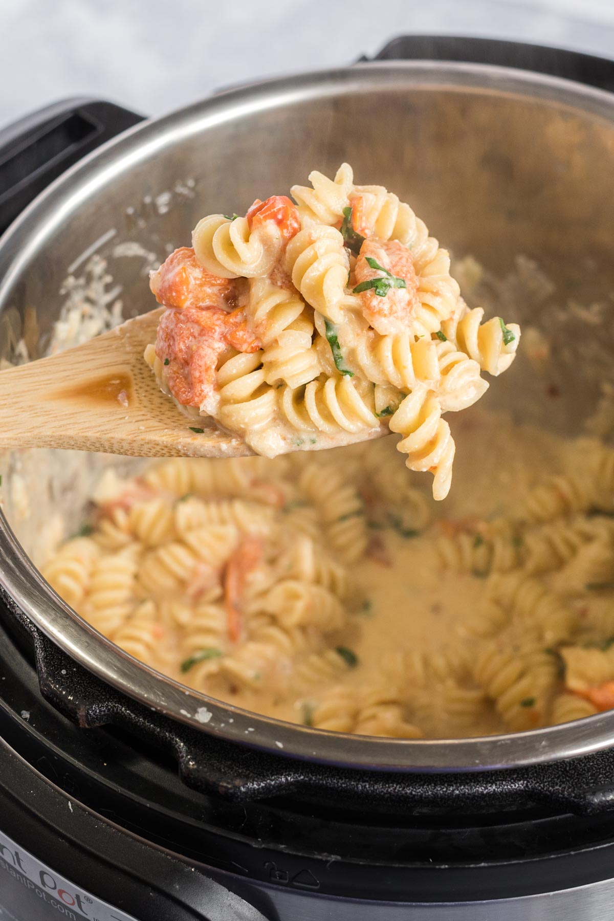 Rotini pasta with tomatoes being served from an instant pot on a wooden spoon.