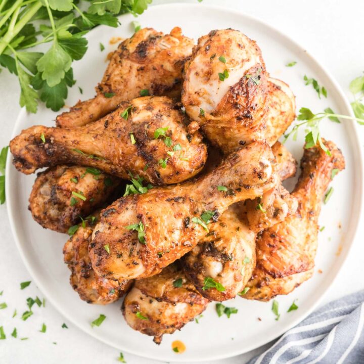 Chicken drumsticks on a white platter garnished with chopped parsley.