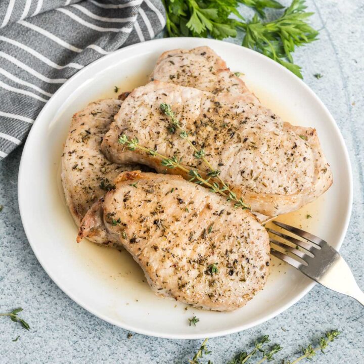 Four cooked pork chops on a white plate garnished with fresh thyme.