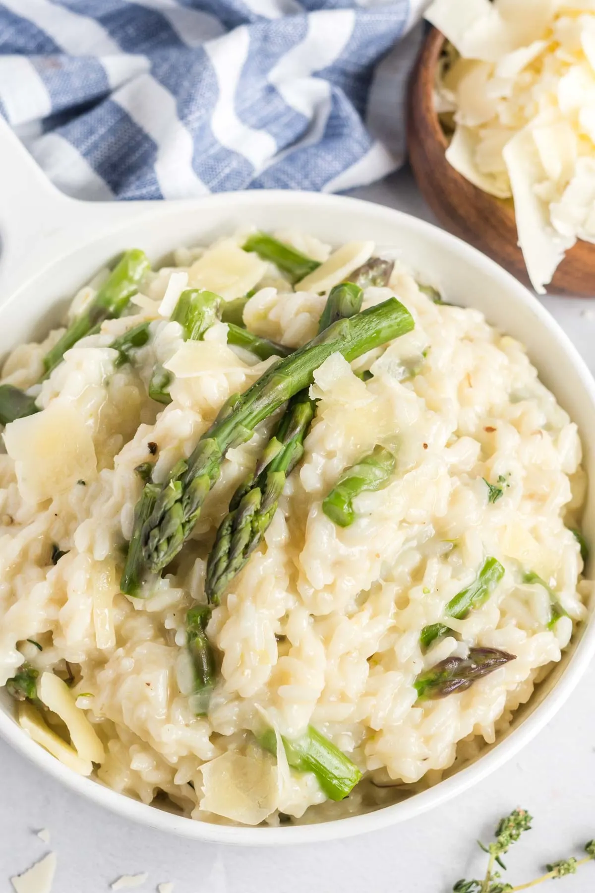 Risotto in a small white dish garnished with asparagus spears and parmesan flakes. 