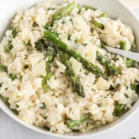 Risotto with asparagus spears in a white bowl with a serving spoon.