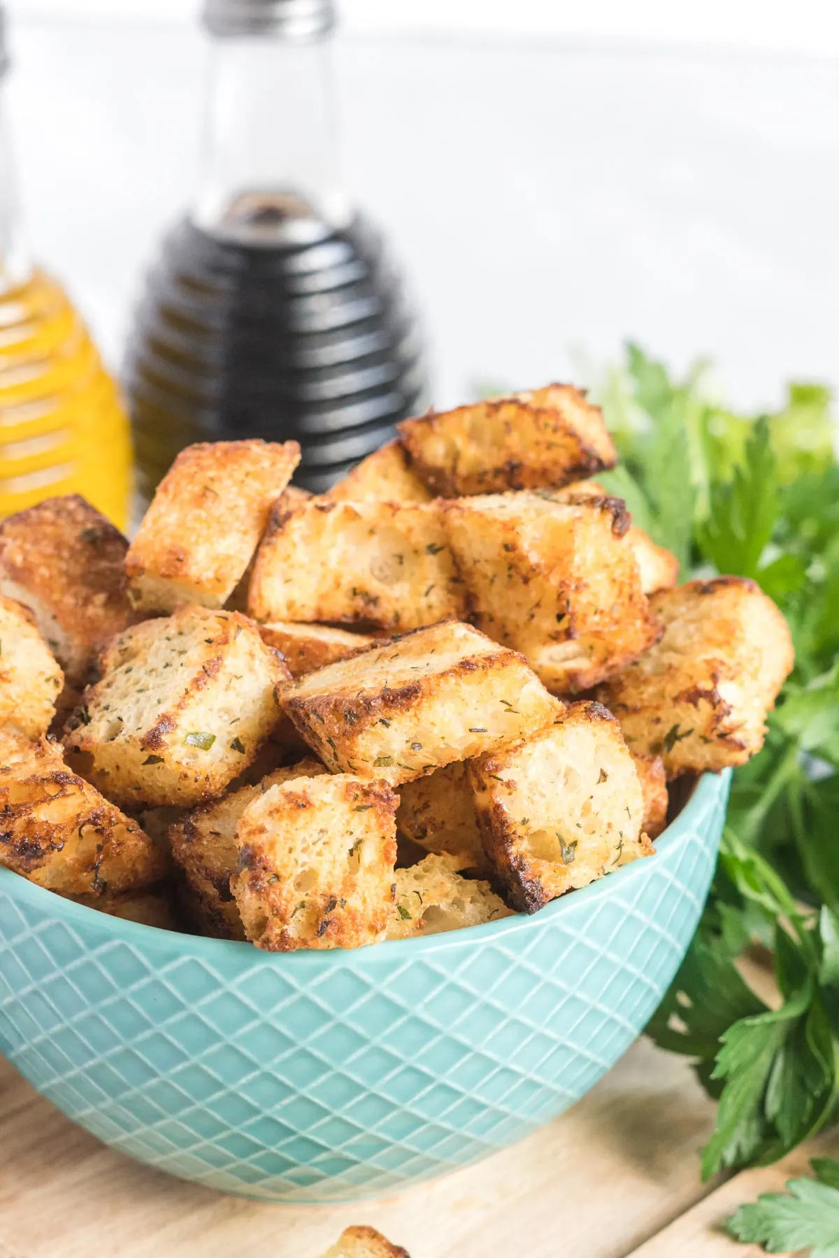 Croutons in a blue ceramic bowl, a bottle of balsamic vinegar and olive oil in the background.