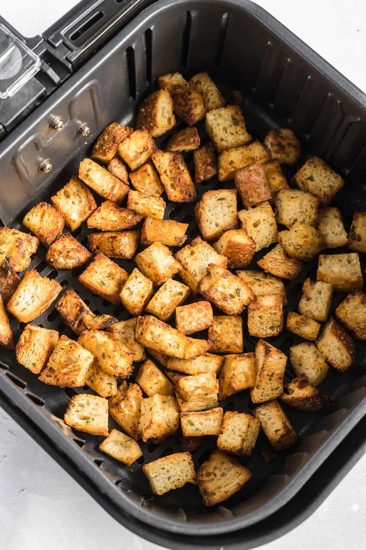 Cooked croutons in an air fryer basket in a single layer.