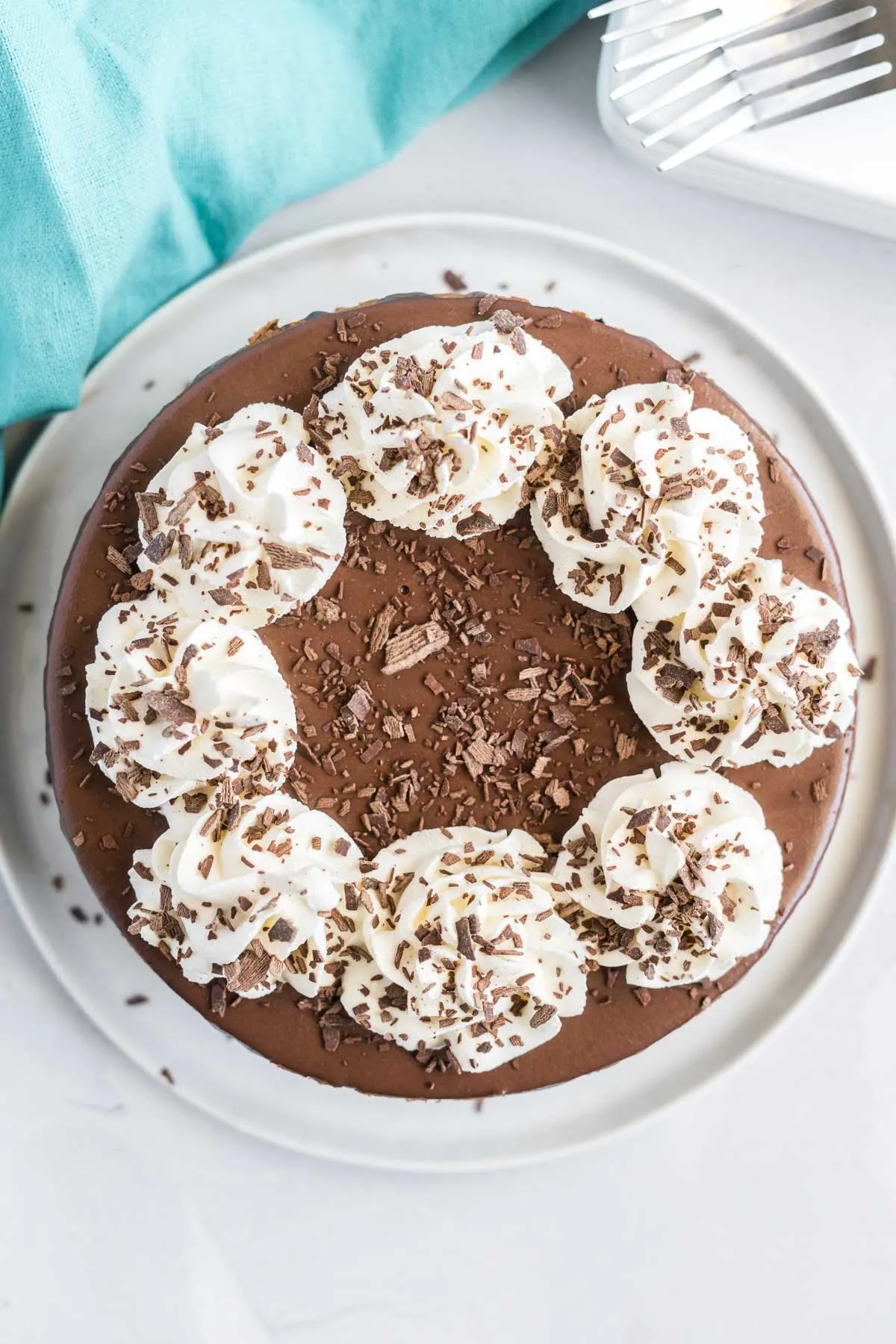 Top view of cheesecake covered in chocolate ganache and decorated with whipped cream swirls and chocolate shavings.