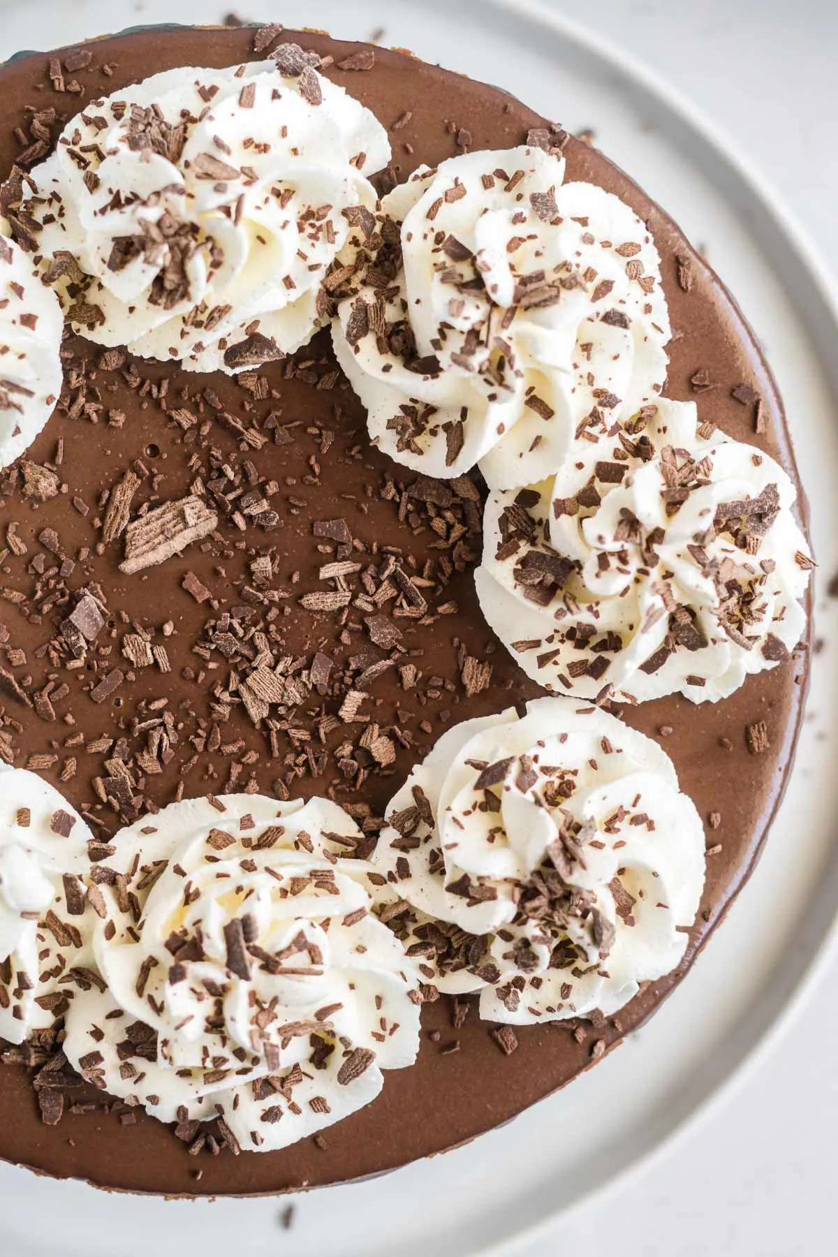 Top view of chocolate cheesecake decorated with whipped cream swirls and shaved chocolate.