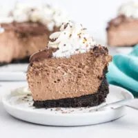 A piece of chocolate cheesecake topped with whipped cream and chocolate shavings on a white plate.