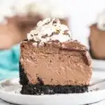 A piece of chocolate cheesecake topped with whipped cream and chocolate shavings on a white plate.