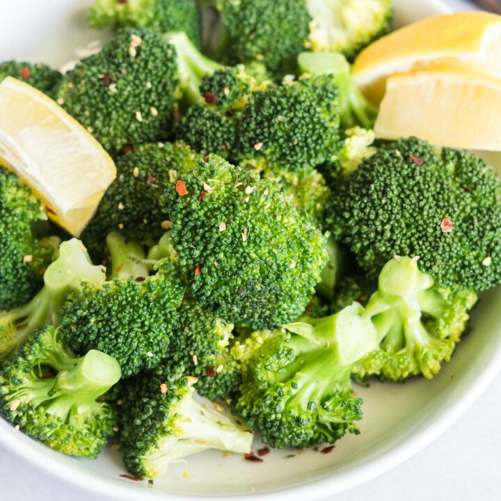 Steamed broccoli in a bowl with lemon wedges and chili flakes.
