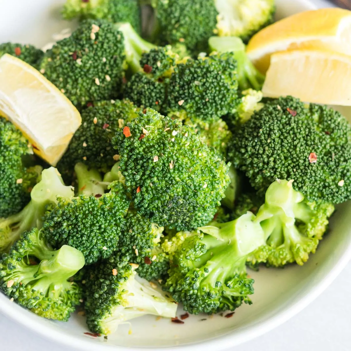 Steamed broccoli in a bowl with lemon wedges and chili flakes.