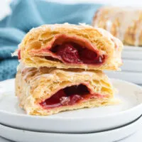 A flaky puff pastry turnover cut in half and filled with cherry pie filling, drizzled with icing.