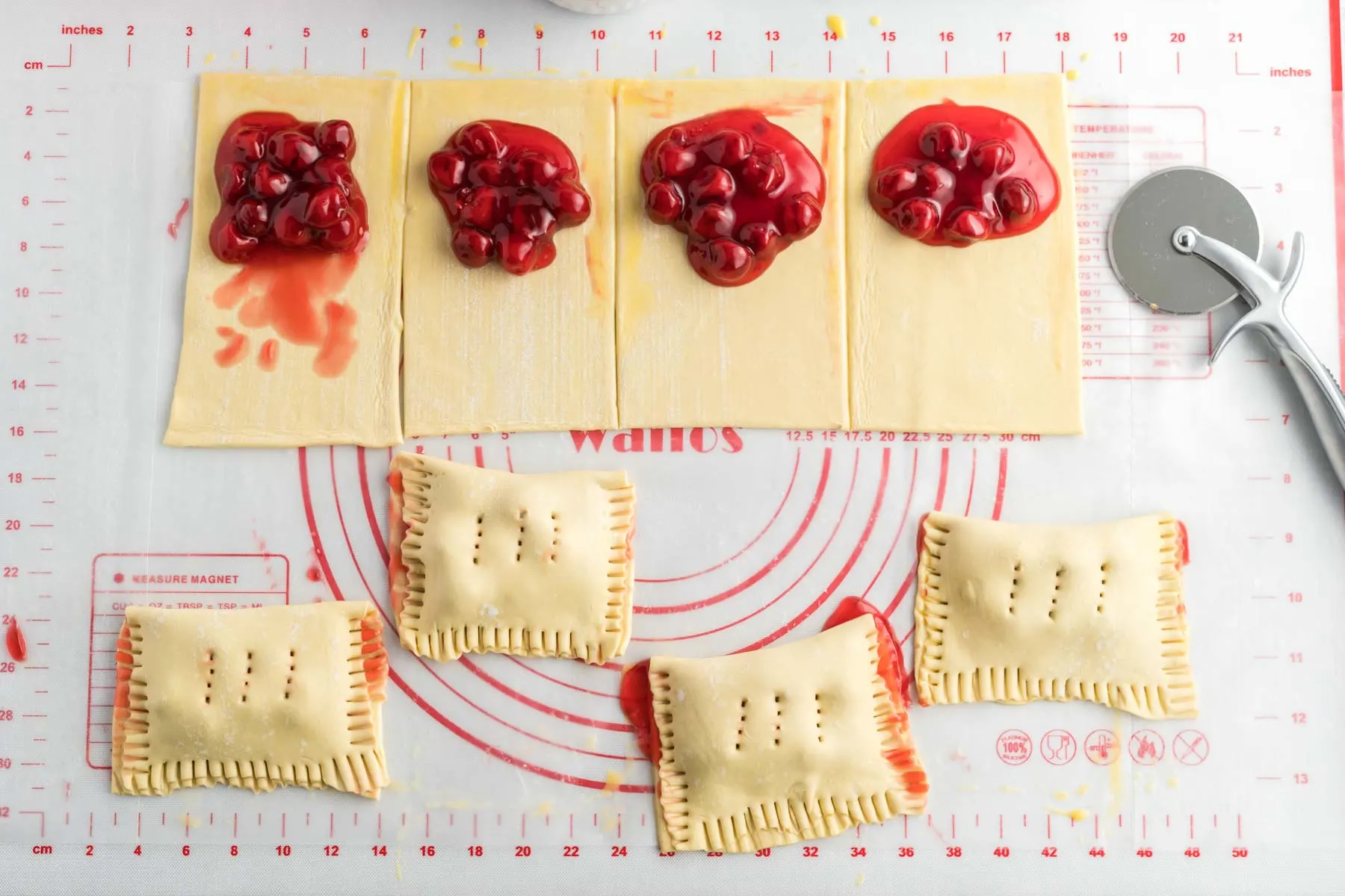 Eight squares of puff pastry with cherry pie filling. Four squares are folded over the cherry pie filling and the edges crimped with a fork.
