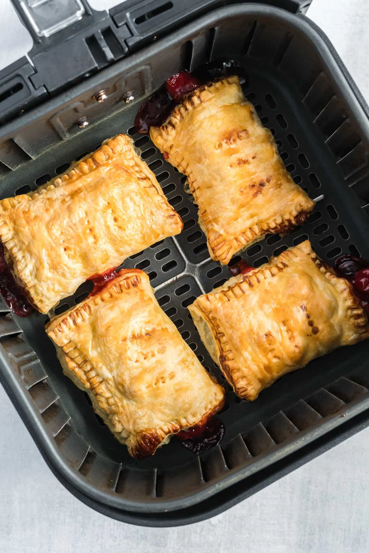 Four turnovers that are puffed and golden brown in an air fryer basket.