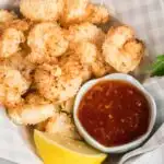 Air fried coconut shrimp in a paper basket with a lemon wedge and a dish of sweet chili dip.