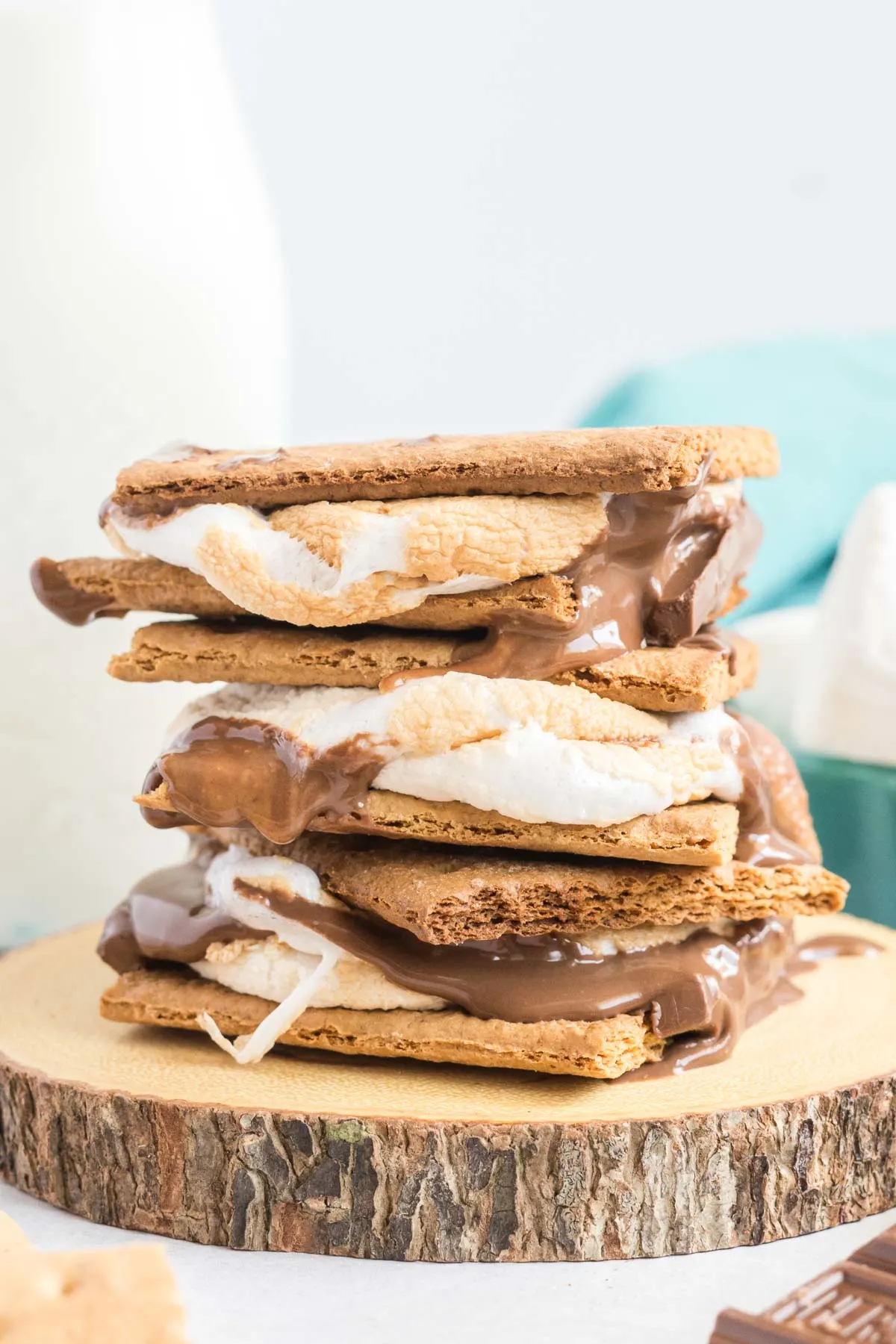 Three smores stacked on a wooden coaster with a bottle of milk beside it.