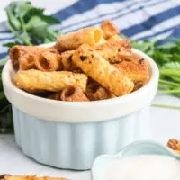 Crispy rigatoni pasta in a blue dish with a small dish of garlic dip on the side.