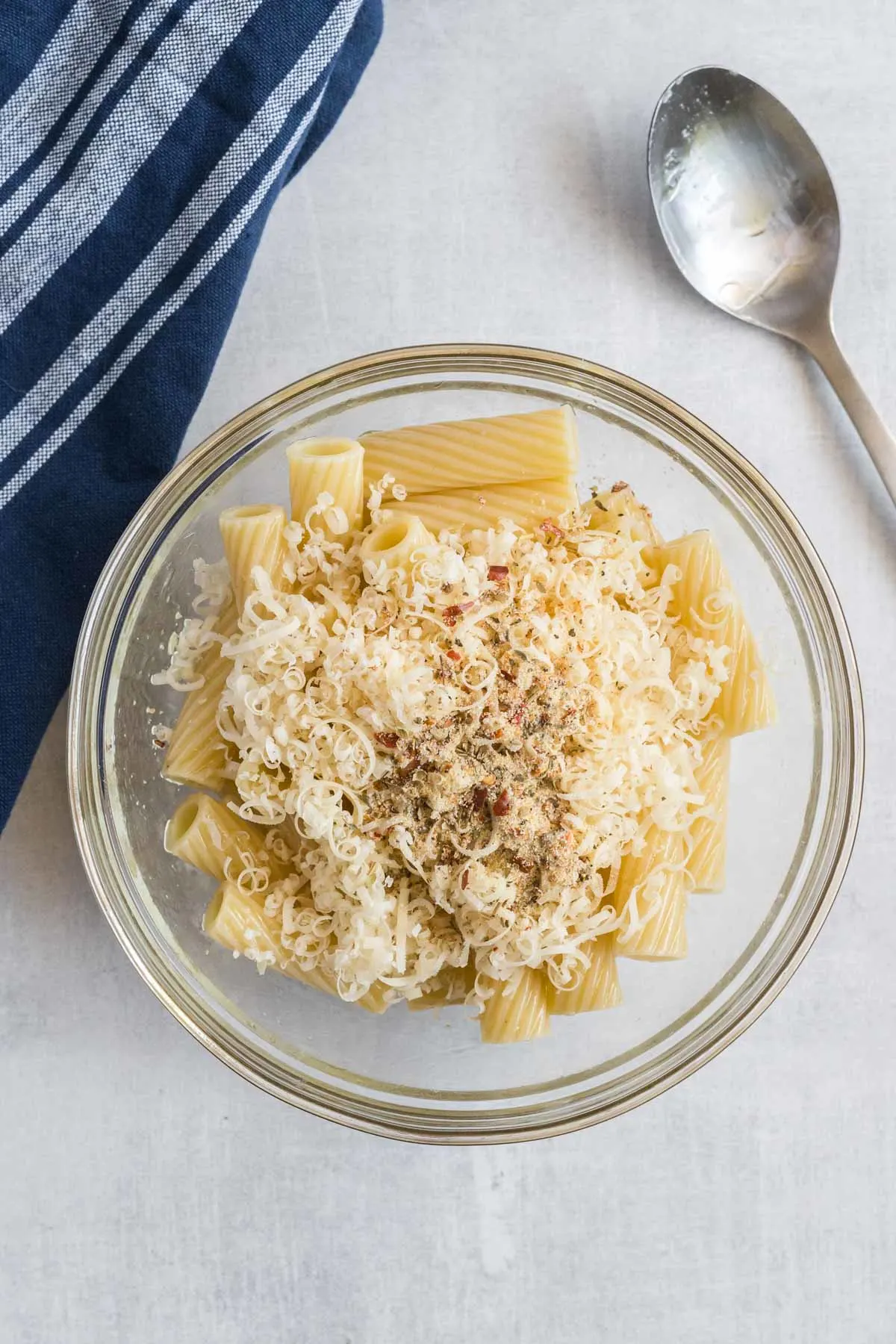 Cooked rigatoni, parmesan cheese, olive oil and seasoning mixed in a small bowl. 