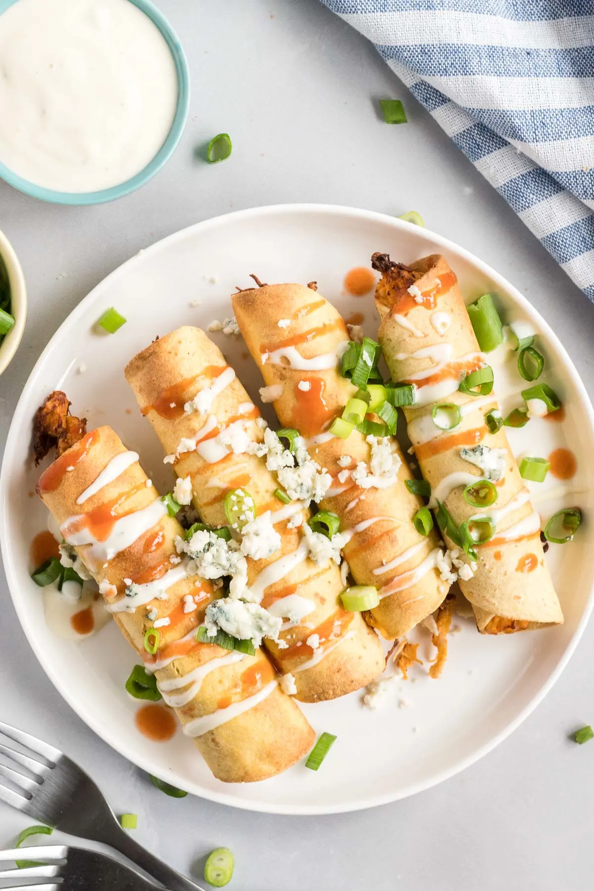 Four taquitos on a plate topped with hot sauce, blue cheese and green onions.