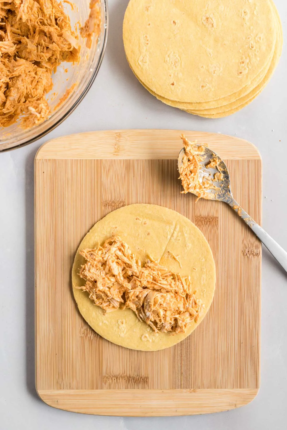 Small tortilla on a cutting board with chicken spread down the middle.