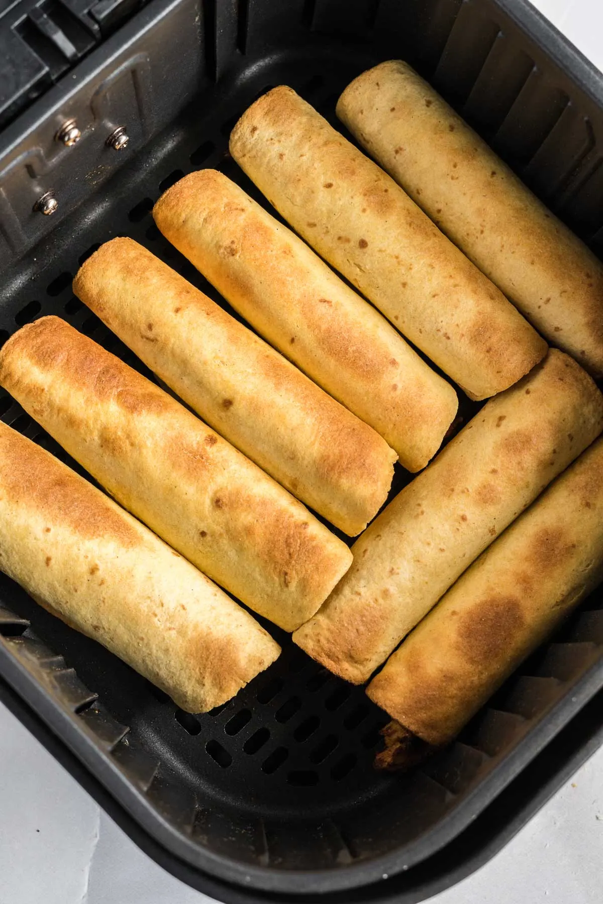 Cooked taquitos in a single layer in an air fryer basket.