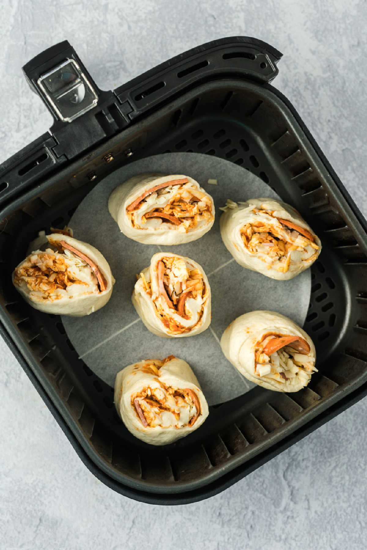 Six unbaked pizza rolls in an air fryer basket with parchment paper underneath.