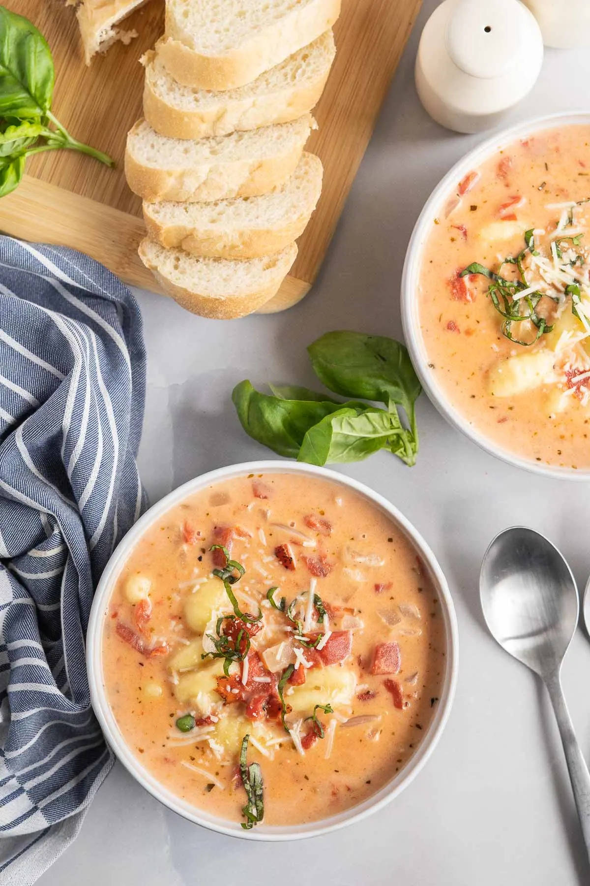 Bowls of soup with sliced fresh bread, herbs and salt and pepper on the side.