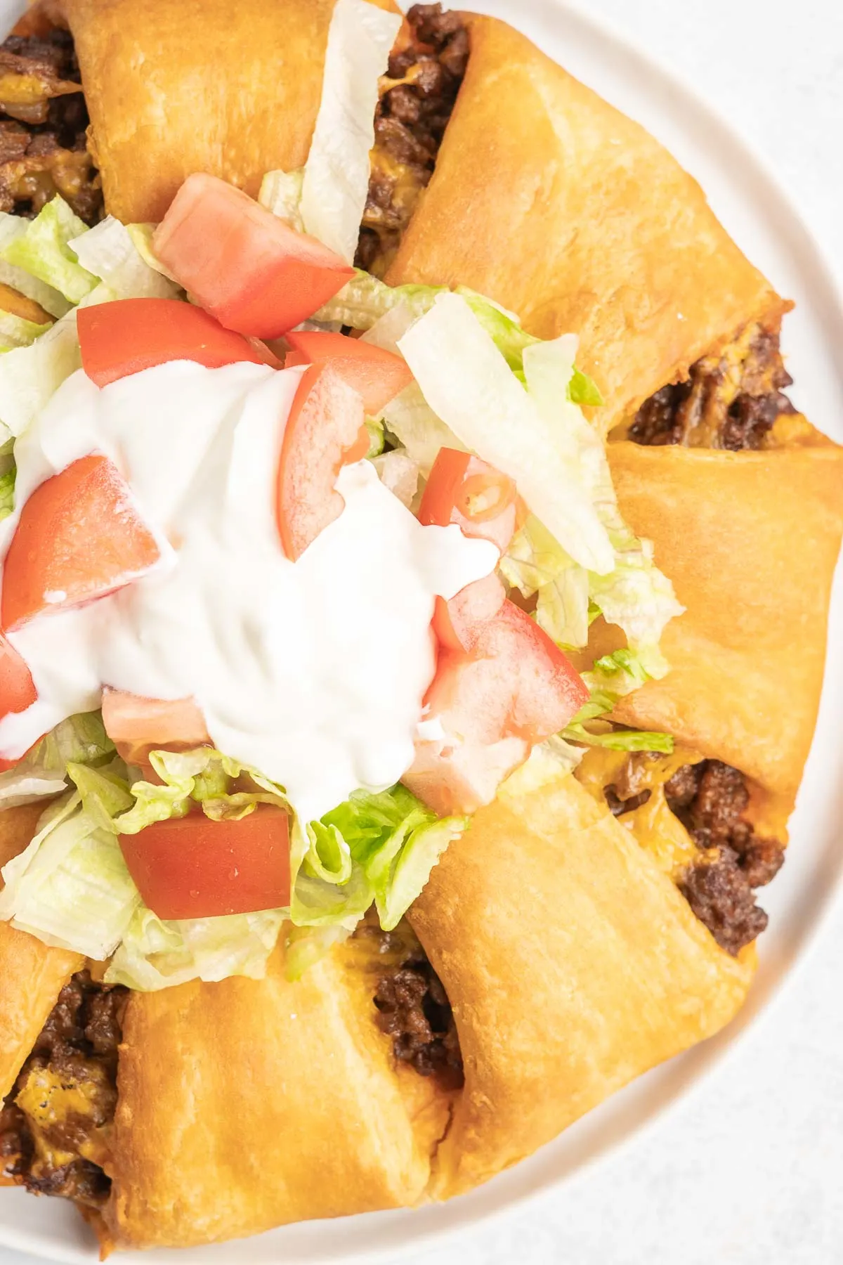 Close up of baked taco ring with lettuce, sour cream and tomato.