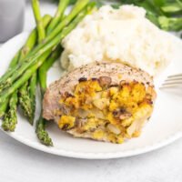 Cornbread stuffed pork chop on a plate with mashed potatoes and asparagus.