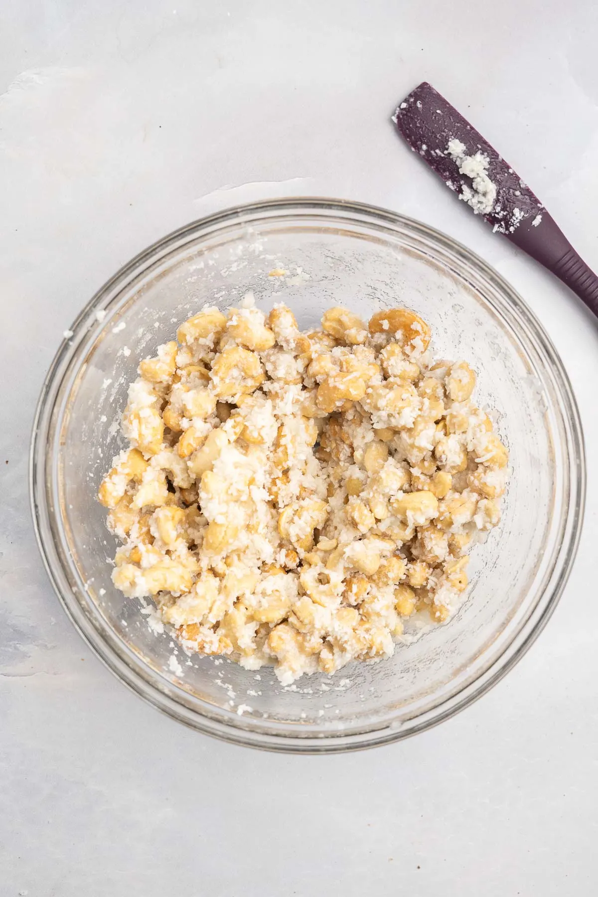 Cashews in a glass bowl coated in egg white, sugar and coconut. 