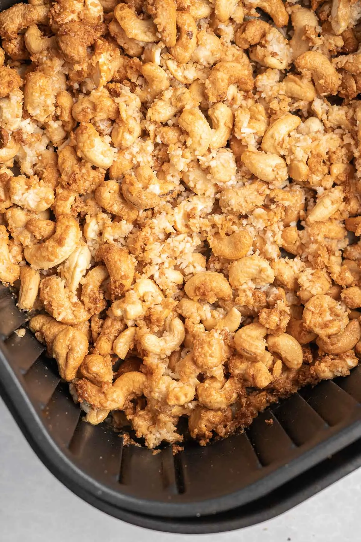 Roasted coconut cashews in an air fryer basket. 