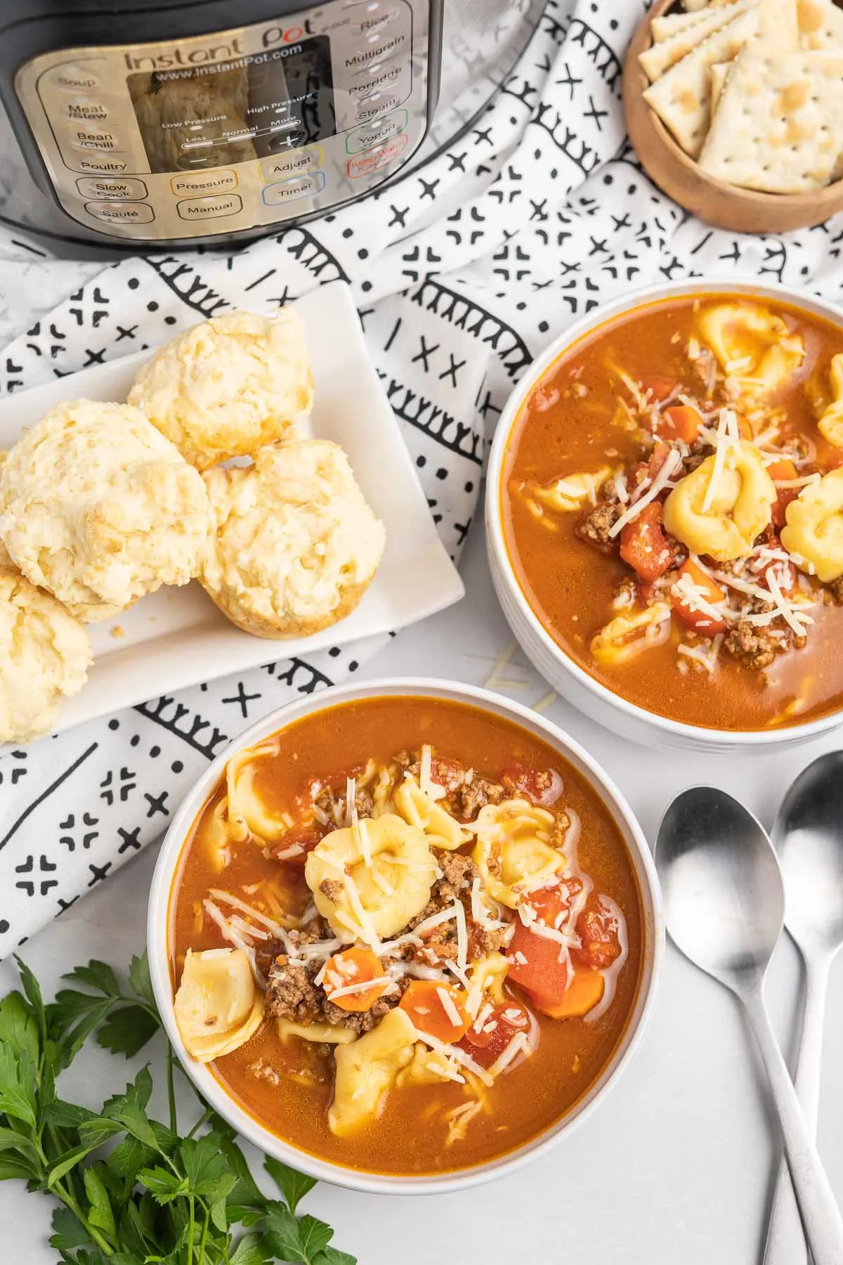 Two bowls of soup and sides of biscuits and crackers. 