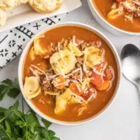 Tortellini soup with ground beef and carrots in a white bowl and a side of biscuits.