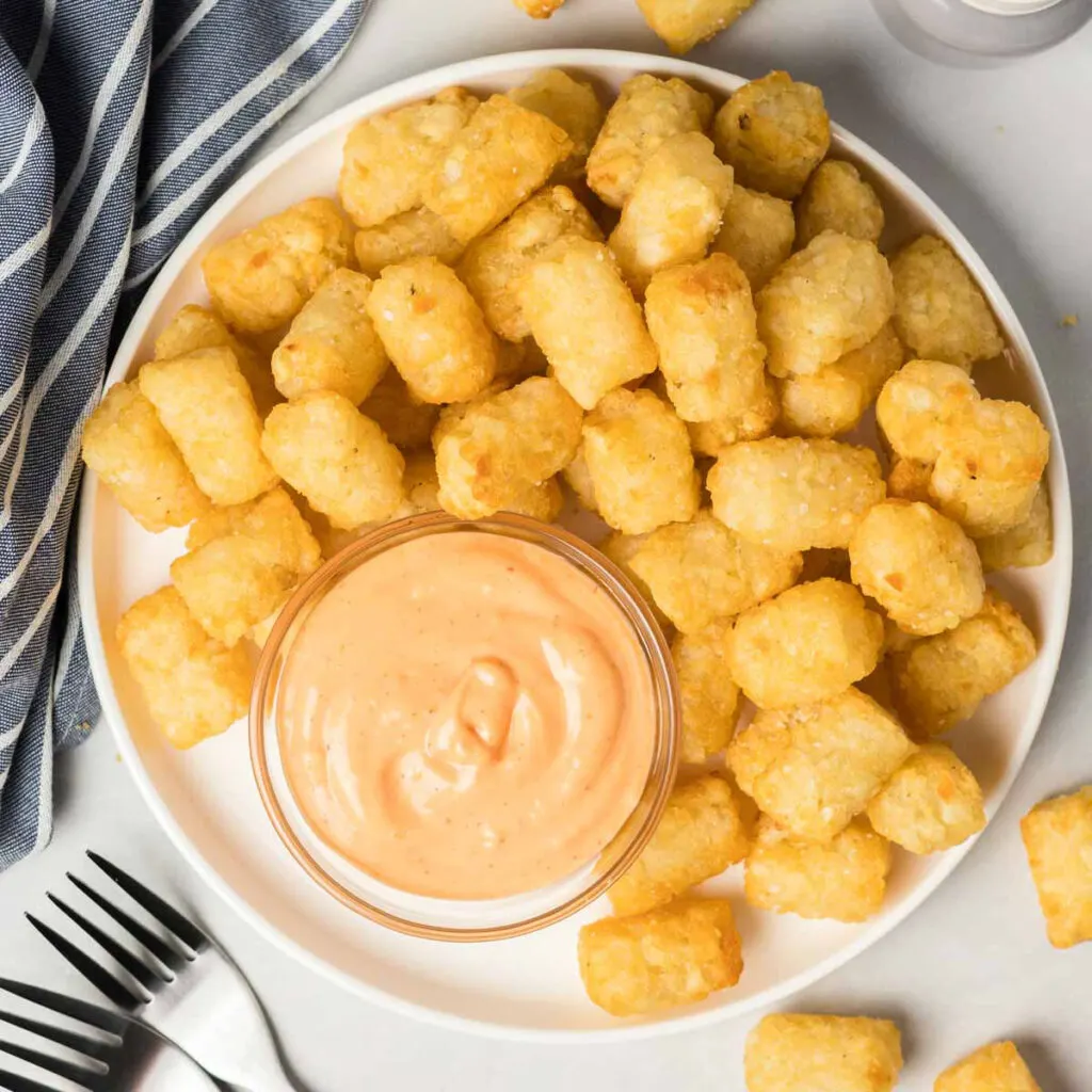 Tater tots on a plate with a dish of sriracha mayo.