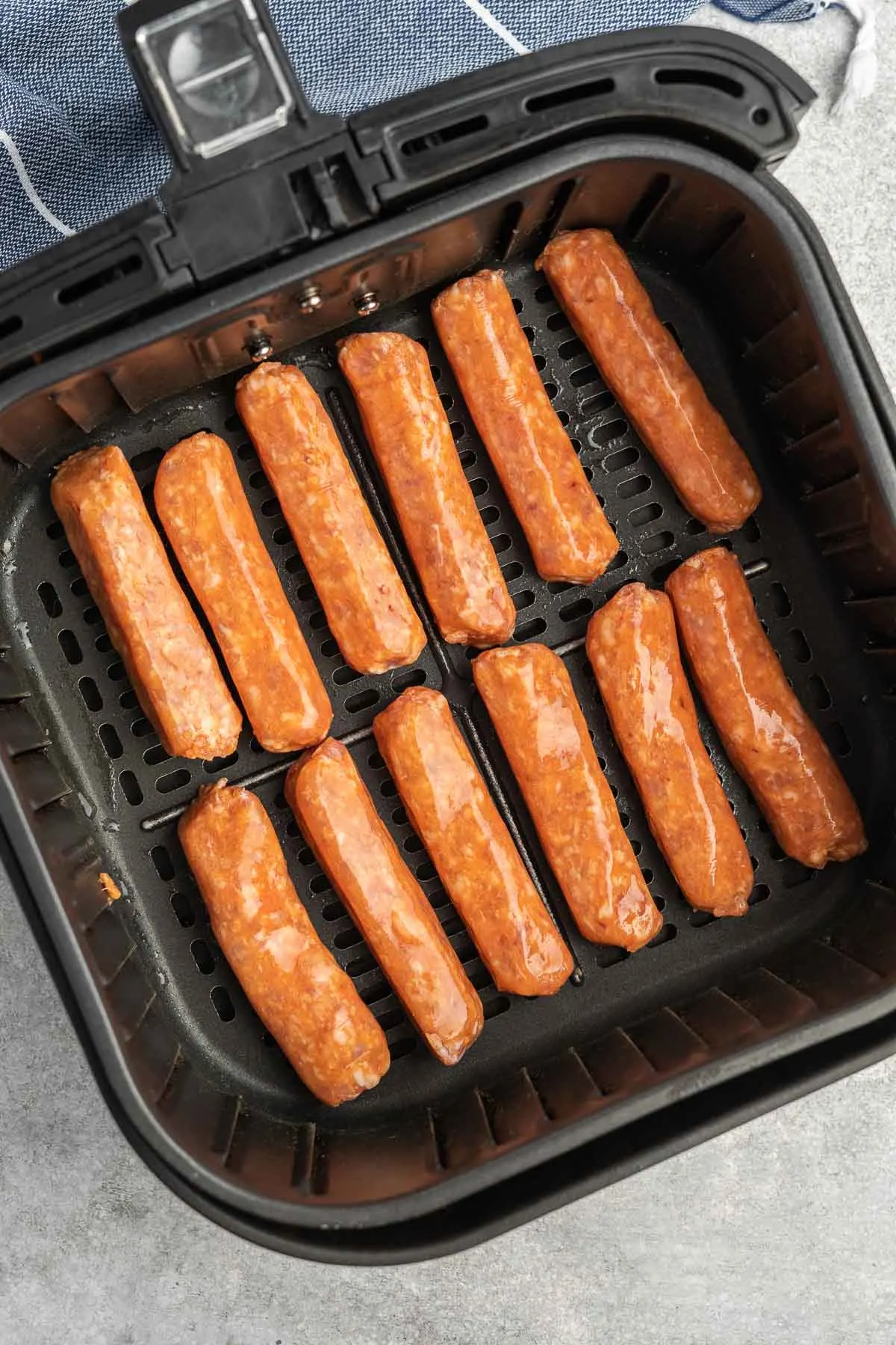 Twelve uncooked sausages in an air fryer basket. 