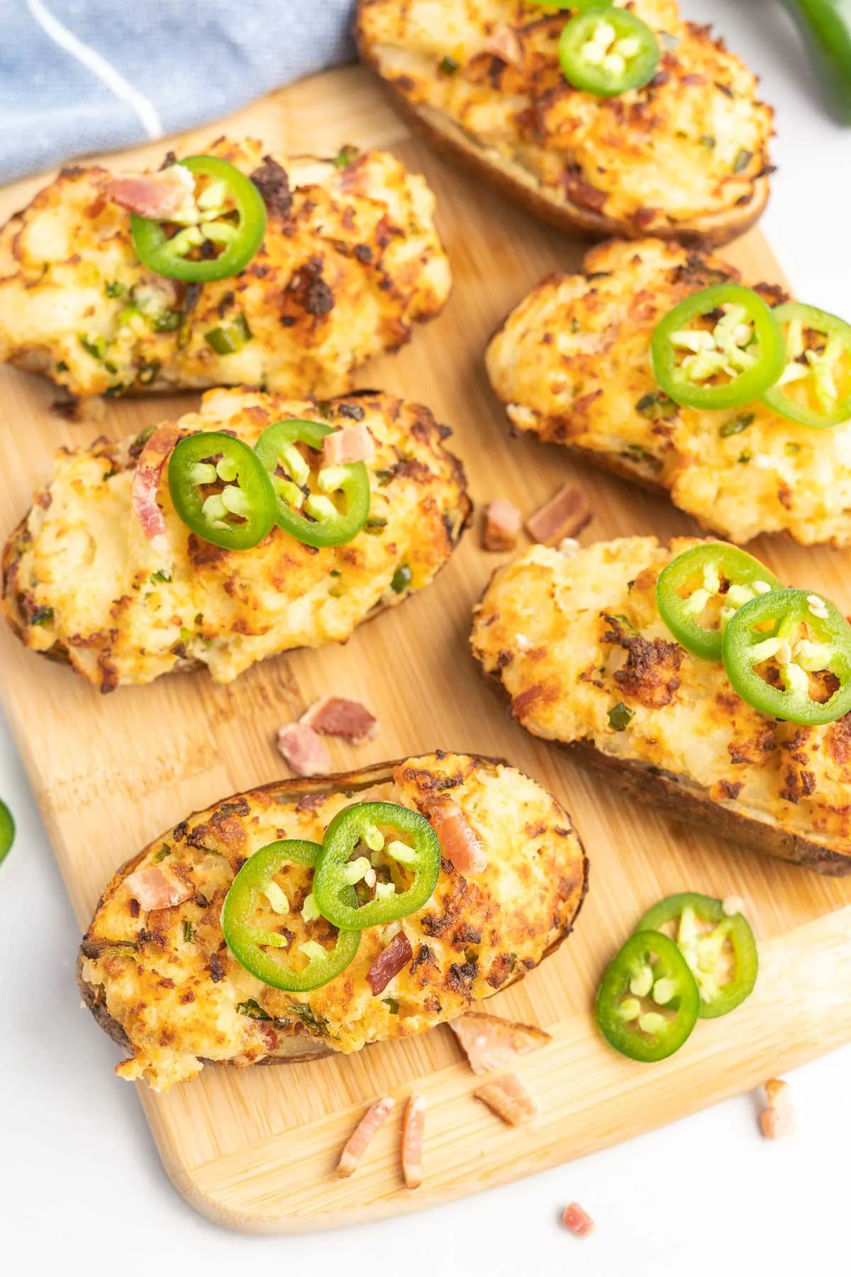 Twice baked potatoes on a wooden board topped with jalapeño slices and chopped bacon. 