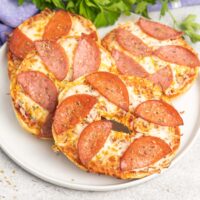 Four pizza bagels on a plate topped with cheese and pepperoni.