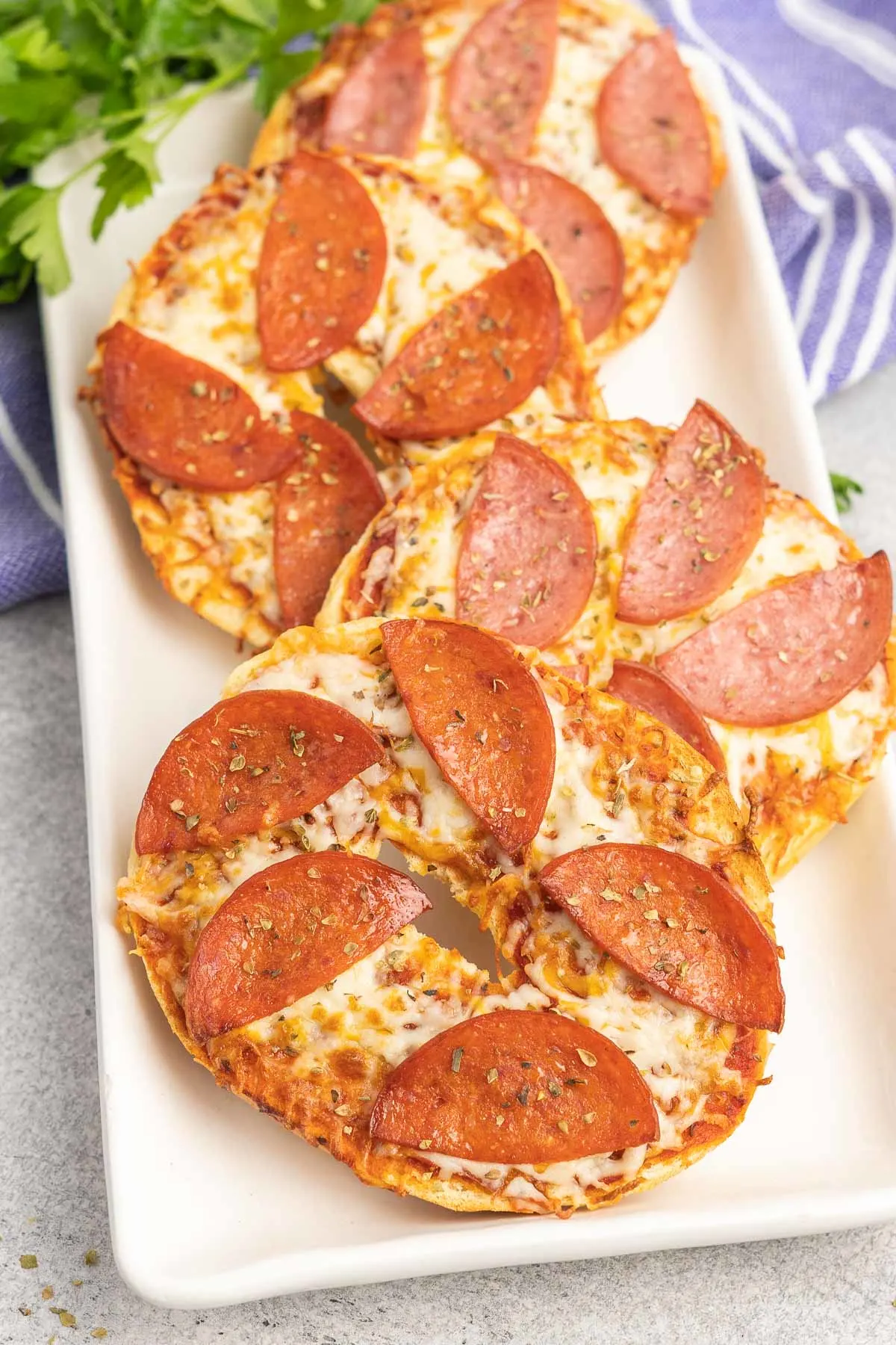 Four pizza bagel halves topped with cheese and sliced meat on a serving platter. 