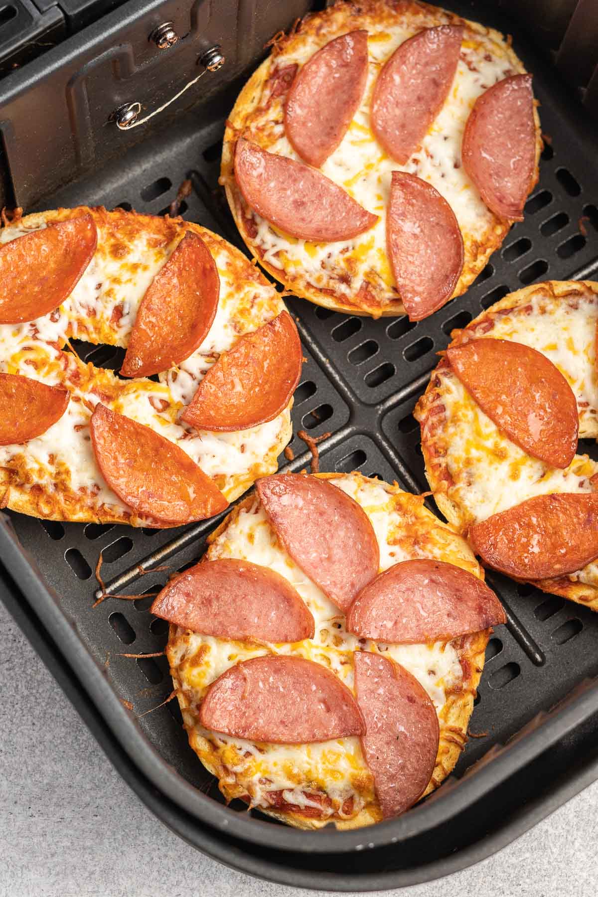 Four pizza bagel halves in an air fryer basket. 