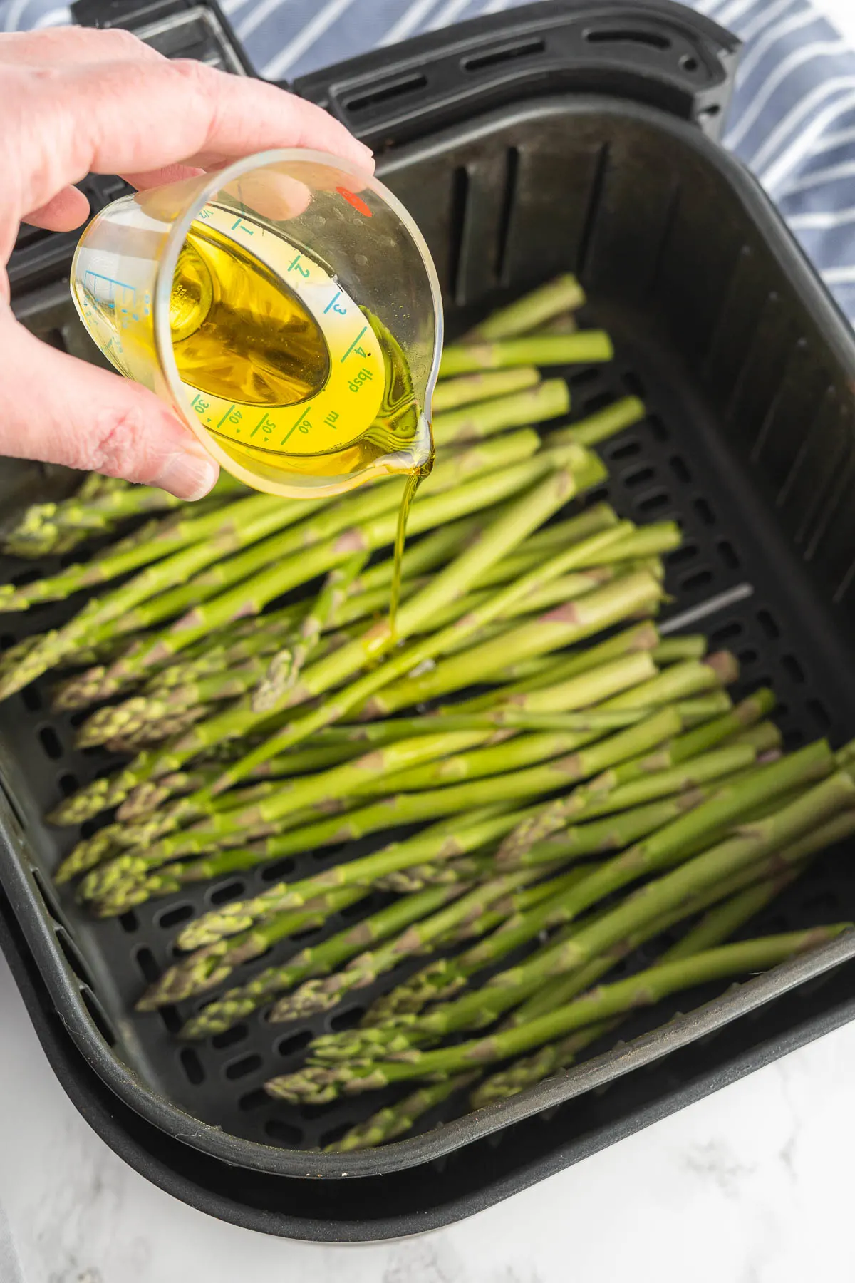 Olive oil drizzled over asparagus in an air fryer basket.