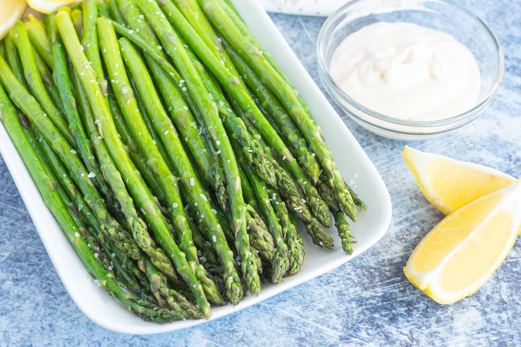 Asparagus sprinkled with salt and a dish of garlic dip and lemon wedges. 