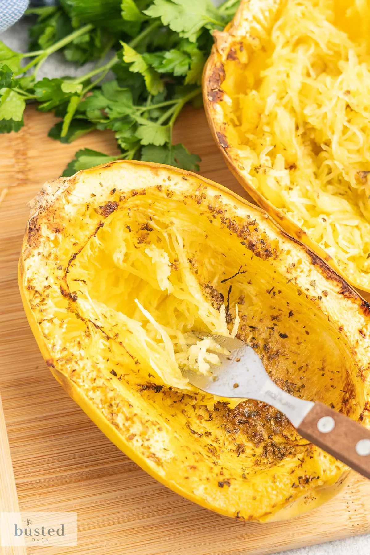 Cooked spaghetti squash half on a cutting board with a fork being dragged through it creating strands. 