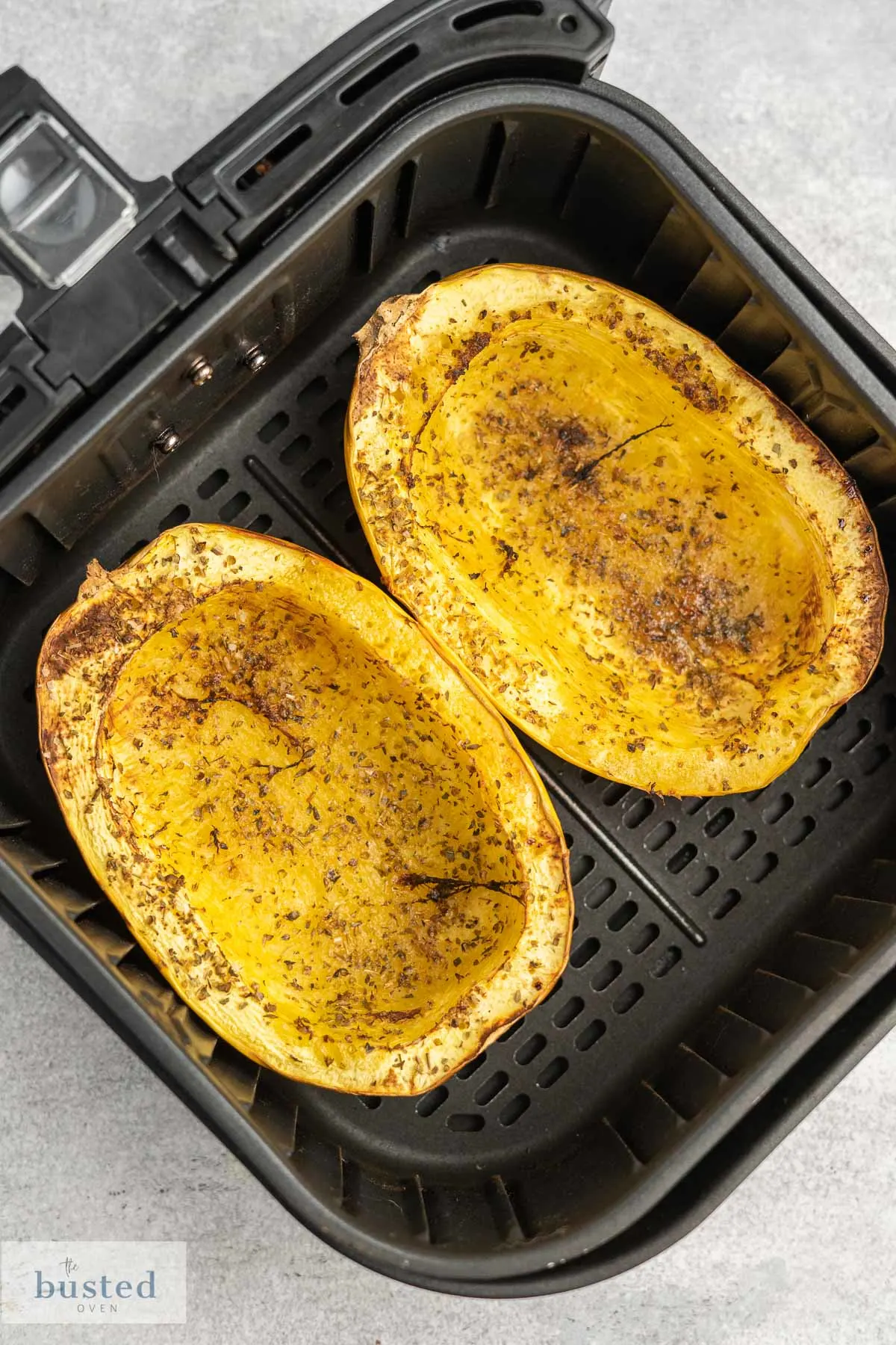 Two cooked spaghetti squash halves in an air fryer basket. 