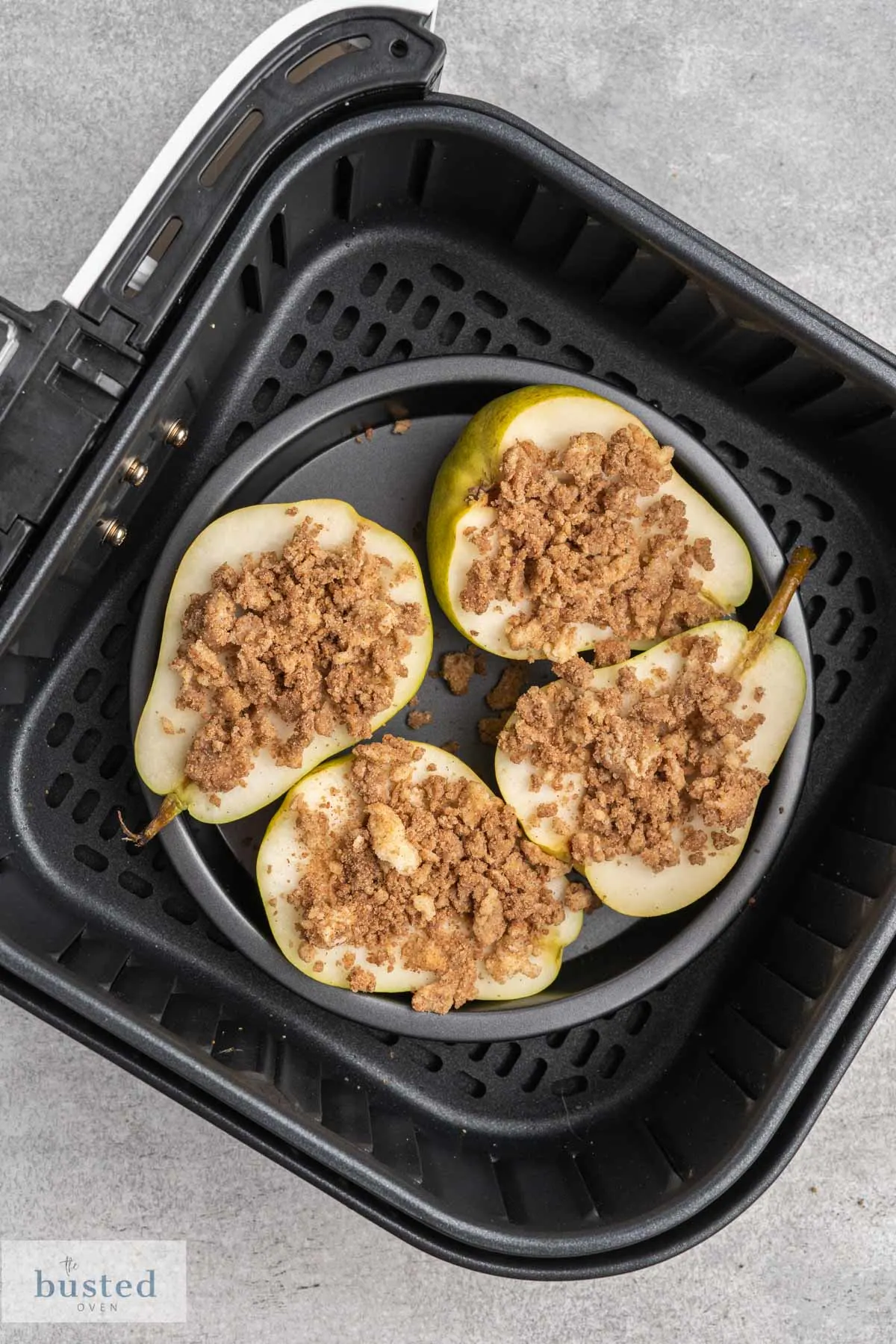 Four pear halves face up with brown sugar cinnamon mix sprinkled on top in a small dish in an air fryer basket.