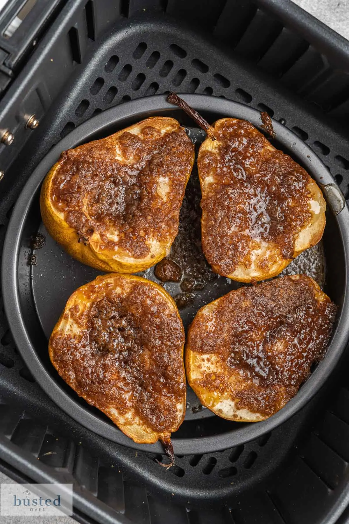 Four pear halves with melted brown sugar and cinnamon in an air fryer basket.