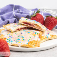 Pop tarts on a plate with one cut in half showing strawberry jam centre.