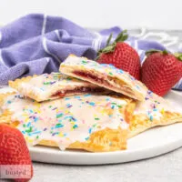 Pop tarts on a plate with one cut in half showing strawberry jam centre.