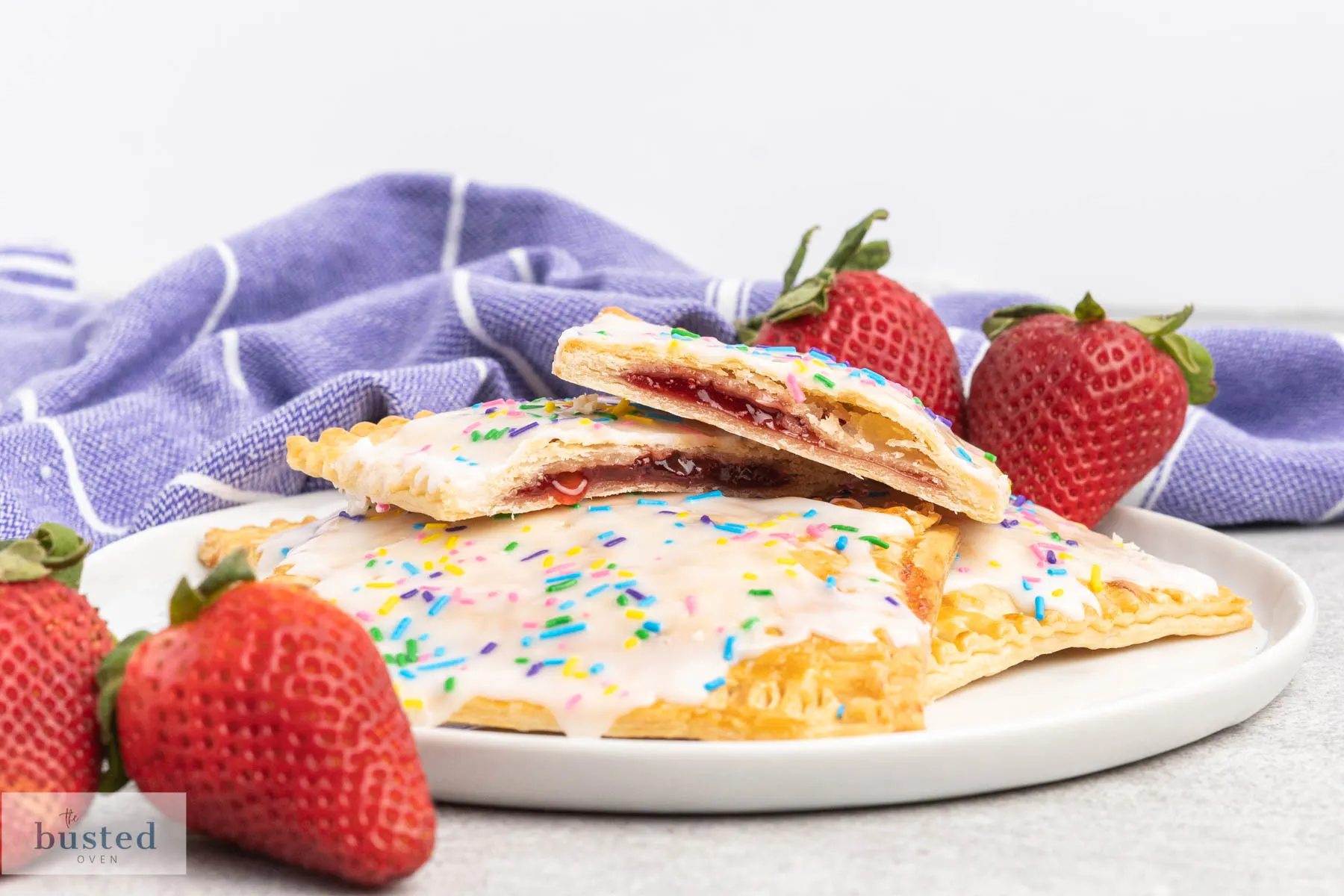 Pop tarts on a plate with white icing and rainbow sprinkles, one cut in half showing strawberry jam in the middle.