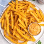 A plate of French fries and a small dish of spicy dip.