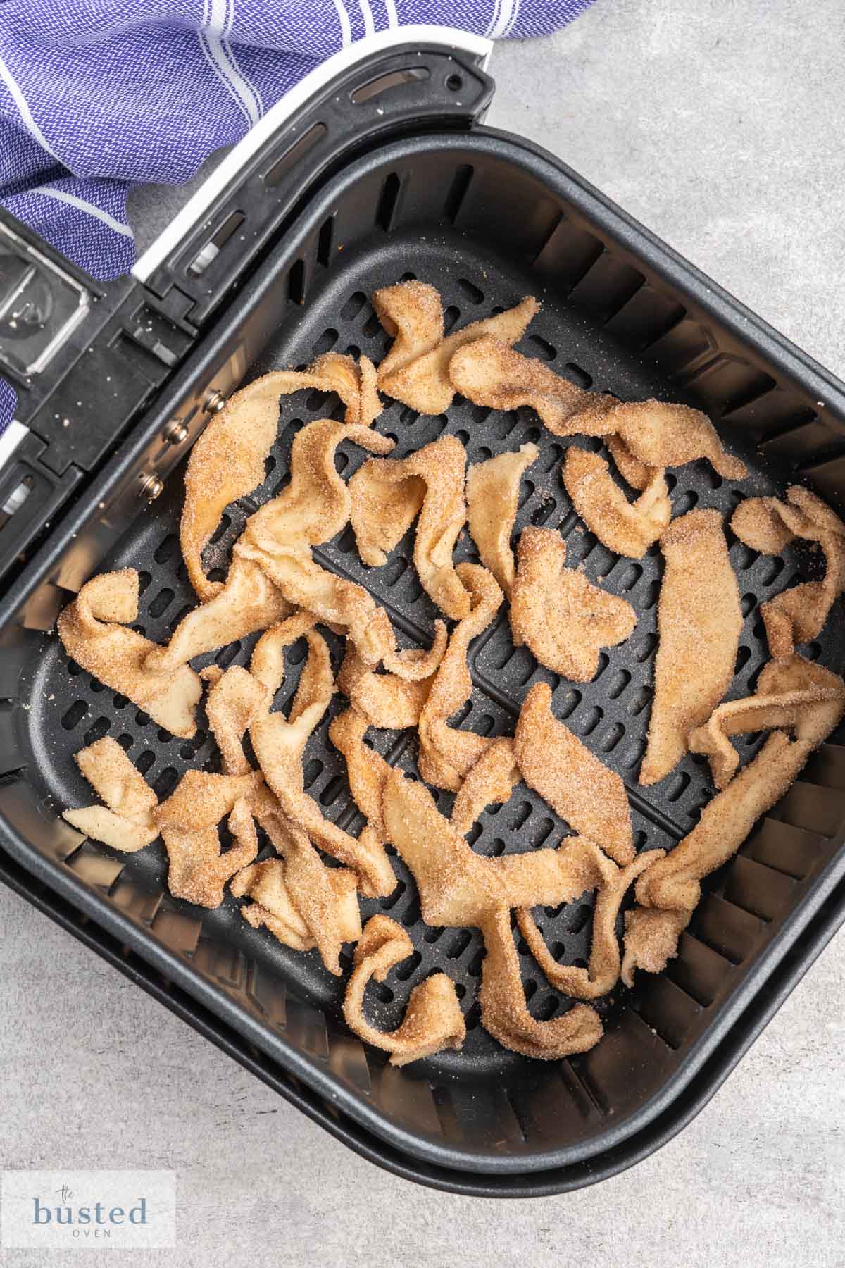 Raw pastry strips coated in cinnamon sugar in a single layer in an air fryer basket. 