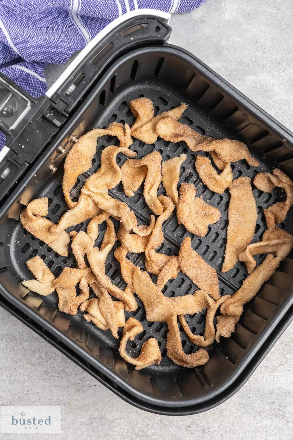 Raw pastry strips coated in cinnamon sugar in a single layer in an air fryer basket.