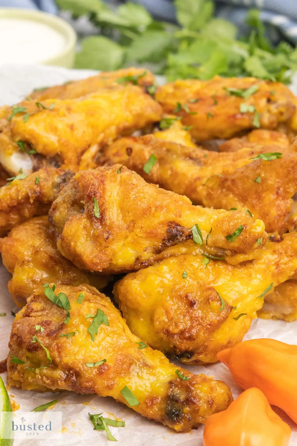 A platter of hot wings with whole habaneros and lime wedges on the side.